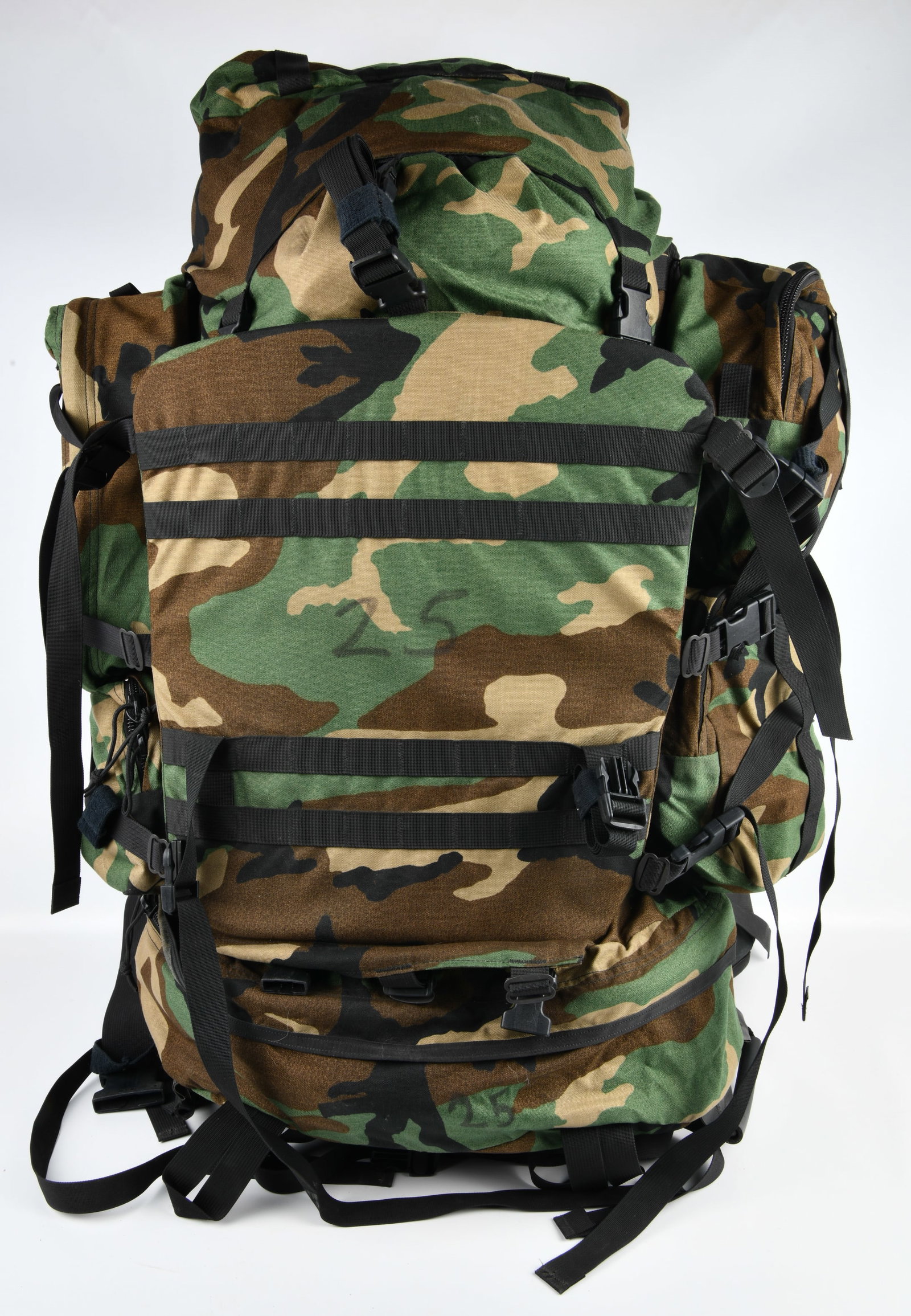 GREGORY SPEAR UM21 Military Rucksack Woodland Camouflage: A GREGORY SPEAR UM21 military rucksack, featuring a woodland camouflage pattern made from a durable synthetic textile, accented with black webbing straps and numerous plastic quick-release buckles. Th