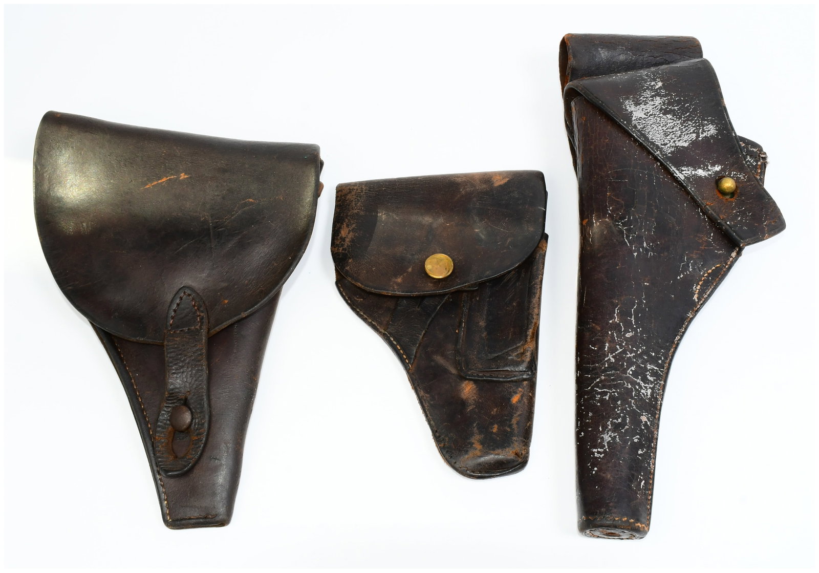 Three Early 20th Century Military Leather Pistol Holsters, including a Rock Island Arsenal 1906: A group of three dark brown leather military pistol holsters, dating to the early 20th century. The tall, rightmost holster is clearly stamped "ROCK ISLAND ARSENAL 1906" and "H.E.K." on its flap, cons