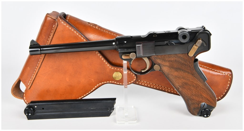 Mauser/Interarms Parabellum American Eagle Luger Semi-Automatic Pistol in 9mm with 6" Barrel: A Mauser/Interarms Parabellum American Eagle Luger Semi-Automatic Pistol in 9mm, featuring a 6" barrel. This dark blued pistol is characterized by its distinctive toggle-lock action, checkered wooden 