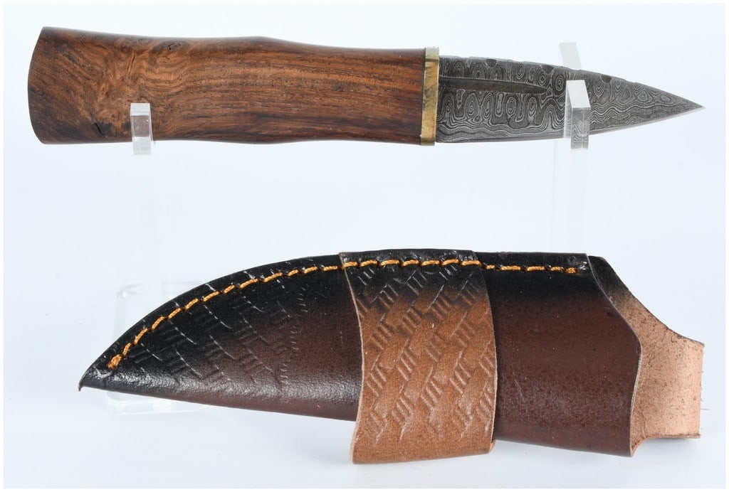 Contemporary Fixed-Blade Hunting Knife with Pattern-Welded (Damascus) Steel Blade and Leather Sheath: A contemporary fixed-blade hunting knife featuring a drop-point pattern-welded (Damascus) steel blade. The blade exhibits a visible central fuller and a partially serrated edge near the hilt, which is