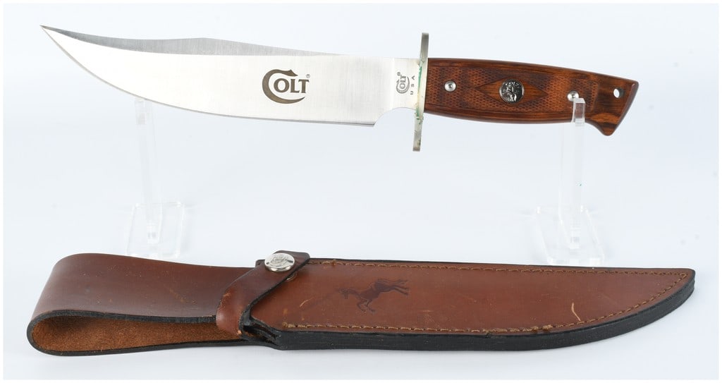 Colt CT1 USA Vintage Bowie Knife with Checkered Wood Handle and Leather Sheath: This lot features a Colt CT1 USA Vintage Bowie Knife, accompanied by its original brown leather sheath. The fixed-blade knife features a stainless steel blade prominently marked with the "COLT" logo o