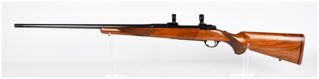 Ruger M77 Bolt-Action Sporting Rifle .338 Win. Mag.: A Ruger M77 bolt-action sporting rifle, chambered in .338 Win. Mag. The rifle features a blued metal barrel and receiver, complemented by a polished wooden stock, likely walnut, which includes checker