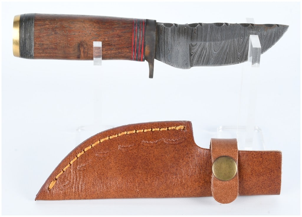 Fixed-Blade Damascus-Style Hunting Knife with Wood Handle and Leather Sheath: A fixed-blade hunting knife featuring a pattern-welded (Damascus-style) steel blade with a prominent wavy texture and jimping along the spine. The handle is crafted from dark, richly grained wood, acc