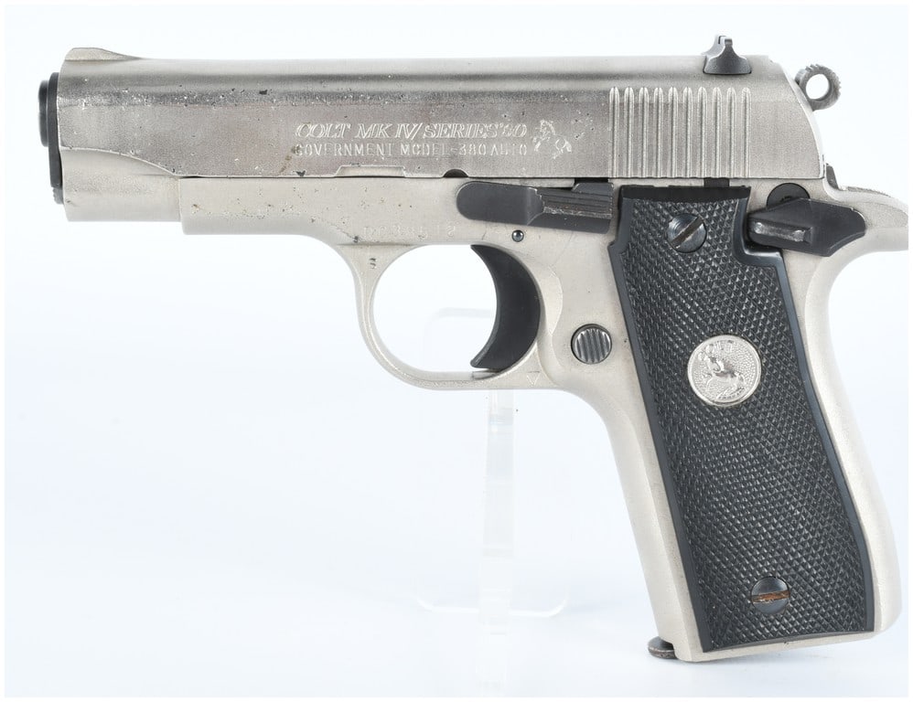 Colt MK IV Series 80 Government Model .380 Auto Semi-Automatic Pistol: A Colt MK IV Series 80 Government Model .380 Auto semi-automatic pistol, featuring a silver-toned metal finish, likely stainless steel or nickel-plated, complemented by black textured grip panels, eac