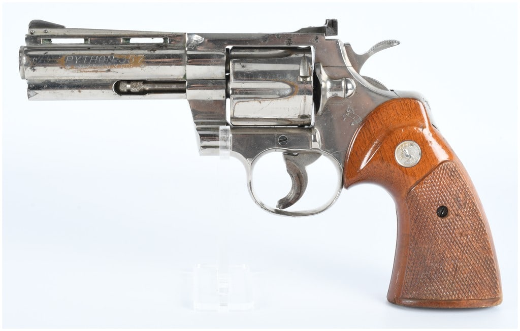 Colt Python .357 Mag Revolver: A Colt Python .357 Magnum revolver. This firearm features a polished metal finish, likely nickel or stainless steel, and is fitted with checkered wooden grip panels, each incorporating a recessed Colt