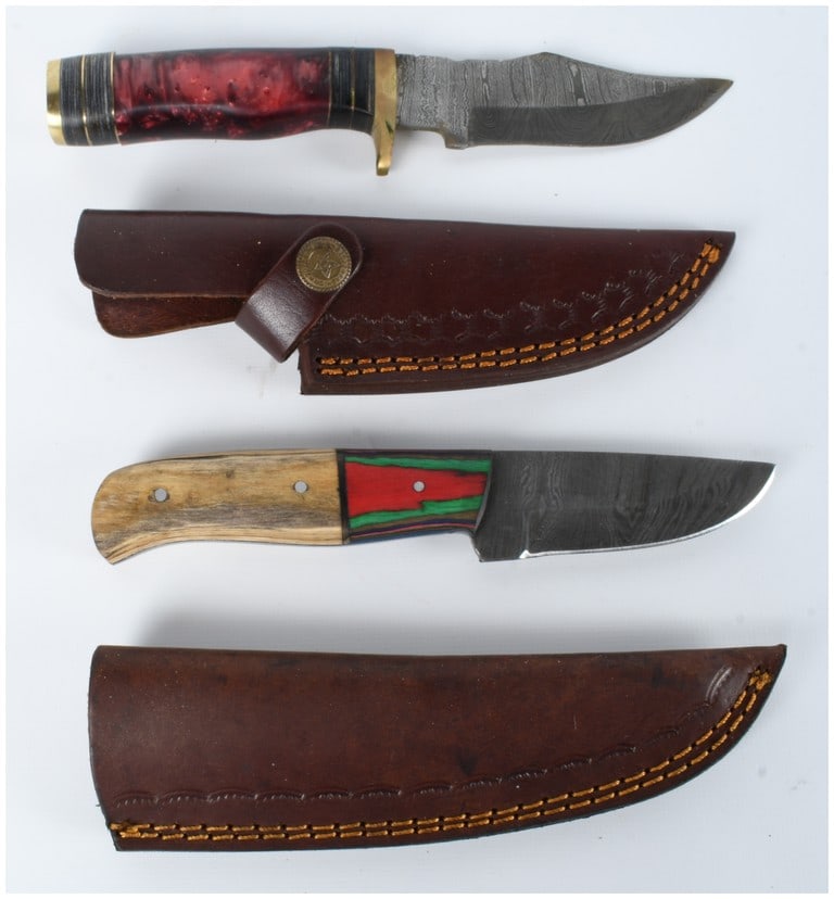Two Damascus Steel Fixed Blade Knives with Leather Sheaths: A lot consisting of two fixed blade knives with Damascus steel blades. The first knife features a clip point profile and a handle of marbled red and black acrylic with brass spacers, guard, and