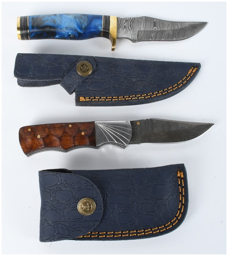 Two Handmade Damascus Steel Knives with Sheaths: Two handmade knives featuring patterned Damascus steel blades. The first is a fixed-blade knife with a handle composed of marbled blue and black resin accented by a brass guard and pommel. The second