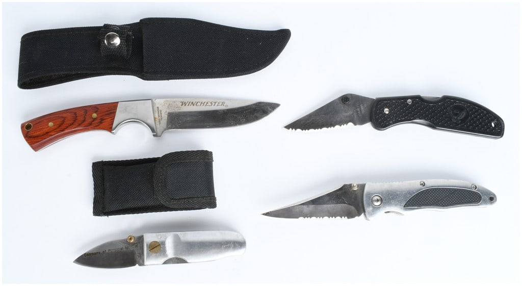 Four Utility and Folding Knives Including Winchester: A group of four modern utility and folding knives. The collection includes a Winchester fixed-blade knife featuring wood-grain handle scales secured by brass pins and a stainless steel blade marked WI