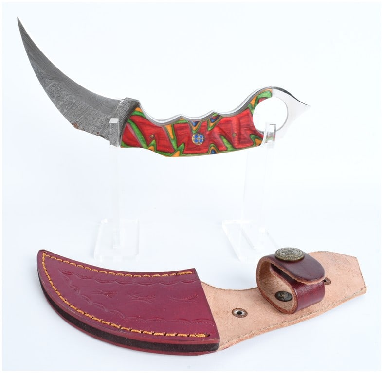 Fixed Blade Damascus Steel Karambit Knife with Laminated Wood Handle and Leather Sheath: This lot consists of one fixed blade karambit-style knife. The blade is constructed of Damascus steel featuring a visible wavy pattern and a curved hawkbill profile. The knife utilizes full tang