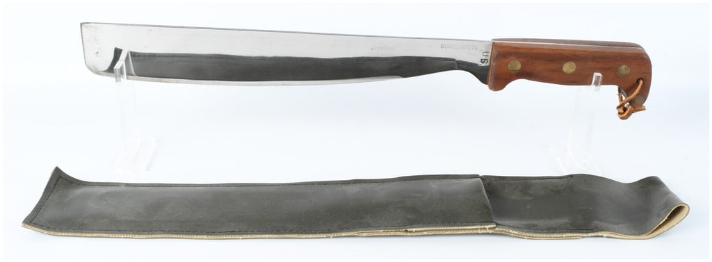 Ontario Knife Co. U.S. Military Machete with Canvas Sheath: This is a fixed blade machete manufactured by the Ontario Knife Co. The blade is constructed of carbon steel and features a wide, single-edged profile with a squared-off tip. The blade flats exhibit a