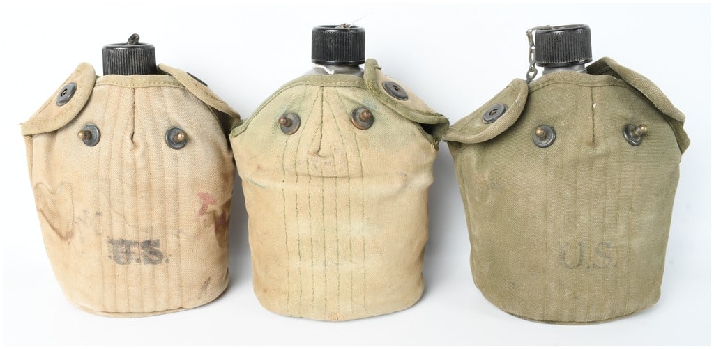 A Trio of U.S. Military M1910 Pattern Canteens and Canvas Covers: A trio of standard-issue United States military field canteens with insulated canvas covers, representing the M1910 pattern utilized during the World War II and Korean War eras. The lot includes three