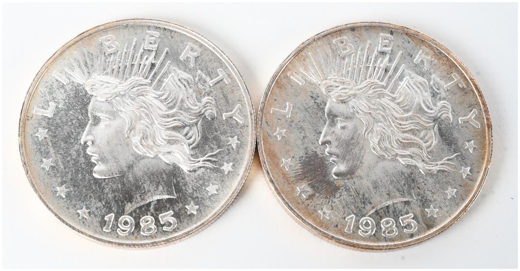 A Pair of 1985 Liberty Silver Trade Unit 1 oz .999 Fine Silver Rounds: A pair of silver bullion rounds, each marked as containing one troy ounce of .999 fine silver. The obverse design features a profile of Liberty in the style of a Peace Dollar, inscribed with LIBERTY a