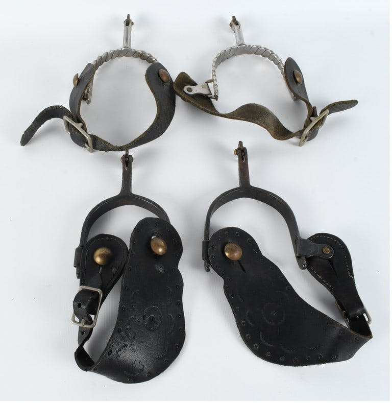 A Collection of Western Style Riding Spurs with Leather Straps: This collection includes multiple western riding spurs of varying designs with associated black leather straps. One pair features silver-toned metal heel bands with a twisted rope design, straight sha