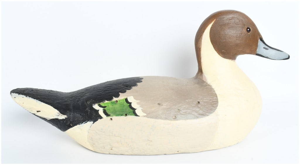 Carved Wood and Textured Cork Northern Pintail Drake Duck Decoy: A carved and painted duck decoy representing a Northern Pintail drake. The decoy features a carved wooden head with inset glass eyes joined to a textured cork body. It is finished in a traditional pin