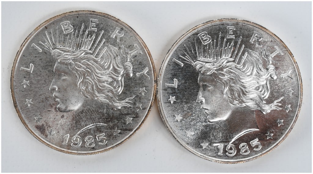 A Pair of 1985 Peace Dollar Design 1 oz t .999 Silver Trade Units: This lot consists of a pair of privately minted silver bullion rounds featuring an obverse design modeled after the United States Peace Dollar. The obverse displays a profile of Liberty wearing a radi