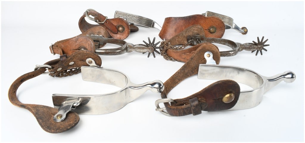An Assortment of Vintage Western Cowboy Spurs: A collection of several pairs of vintage equestrian spurs of varying styles and construction. One pair is composed of polished silver-tone metal featuring rounded ball shanks and weathered leather str