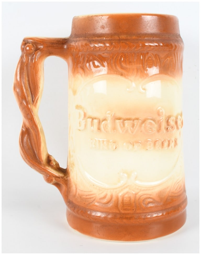 Budweiser King of Beers Relief Stein: This ceramic vessel is consistent with the 1954 Budweiser throw away style beer mug, specifically model BB14. The piece features a two-tone glaze application, with a burnt orange-brown color at the ri