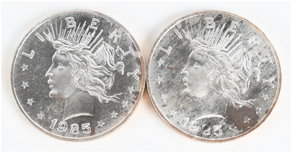 A Pair of 1985 Peace Dollar Design 1 Troy Ounce .999 Silver Trade Units: A pair of private issue silver bullion rounds struck in .999 fine silver. The obverse features a profile of Liberty wearing a radiate crown, modeled after the United States Peace Dollar, with the text