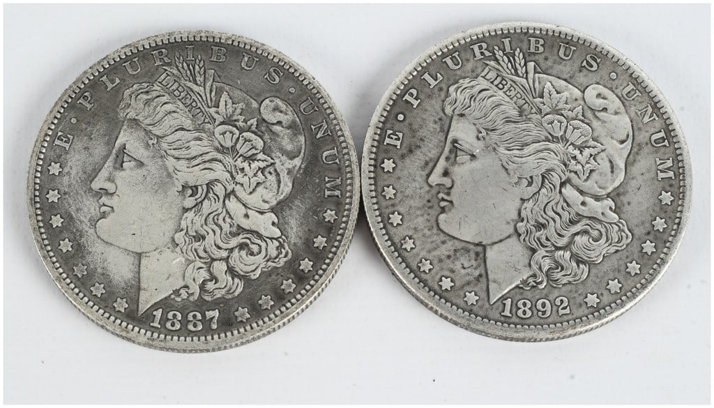 A Pair of US Morgan Silver Dollars, 1887 and 1892: This pair of United States Morgan silver dollars includes specimens dated 1887 and 1892. Both coins are struck in 90% silver and 10% copper. These examples were produced at the Philadelphia mint, as i