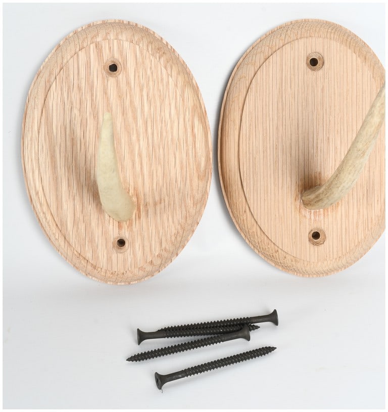 A Pair of John G. Zimmerman Oak and Antler Wall Hooks: A pair of wall-mounted antler hooks manufactured by John G. Zimmerman of Harpers Ferry, West Virginia. Each unit consists of a single natural antler tine secured to an oval-shaped base made of oak. Th