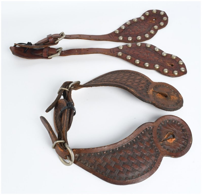 A Collection of Vintage Tooled Leather Western Spur Straps: A collection of vintage Western-style spur straps crafted from medium-brown leather. One set features narrow straps with wide, rounded tabs decorated with a central stamped basketweave pattern and a b