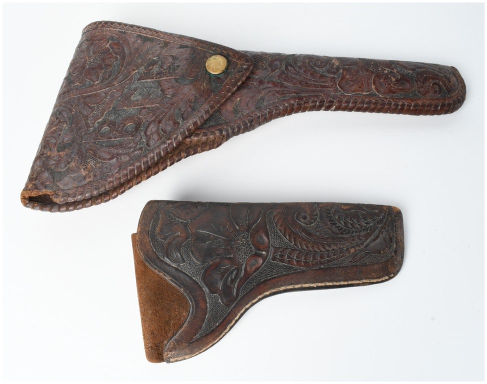A Pair of Floral Tooled Leather Holsters Attributed to H.H. Heiser: A pair of hand-tooled leather firearm holsters. The larger specimen is designed for a large-frame revolver and features intricate floral and scroll motifs accented by a decorative whip-stitched border