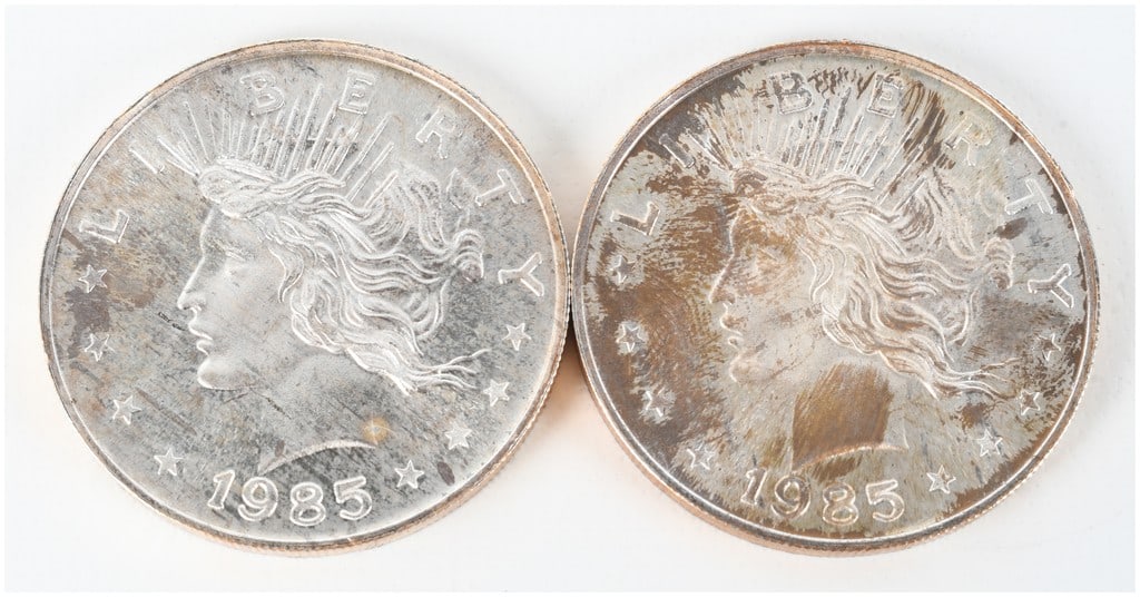 A Pair of 1985 Peace Dollar Design 1 Troy Ounce .999 Fine Silver Trade Units: This lot features two silver rounds, each containing one troy ounce of .999 fine silver. The obverse of each round displays a profile of Liberty inspired by the United States Peace Dollar design, with