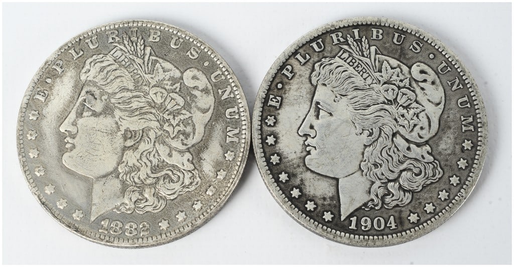 A Pair of US 1882 and 1904 Morgan Silver Dollars: This lot consists of two US Morgan silver dollars dated 1882 and 1904. Both coins are composed of 90% silver and 10% copper. Each features the George T. Morgan obverse and reverse designs. Inscription