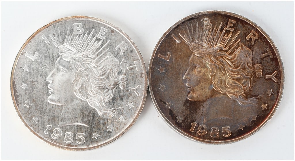 A Pair of 1985 Peace Dollar Style .999 Fine Silver Trade Units: This lot consists of two silver bullion rounds produced by a private mint. Each round features a design inspired by the United States Peace Dollar. The obverse depicts a profile of Liberty with a radi