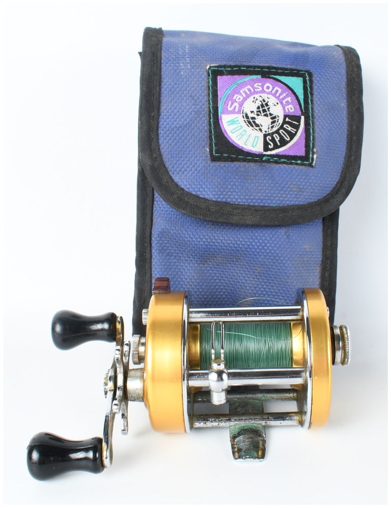 Penn 940 Levelmatic Baitcasting Fishing Reel with Samsonite Pouch: This lot features a vintage Penn 940 Levelmatic baitcasting fishing reel accompanied by a Samsonite World Sport carrying pouch. The reel is constructed with a gold-anodized aluminum frame and side