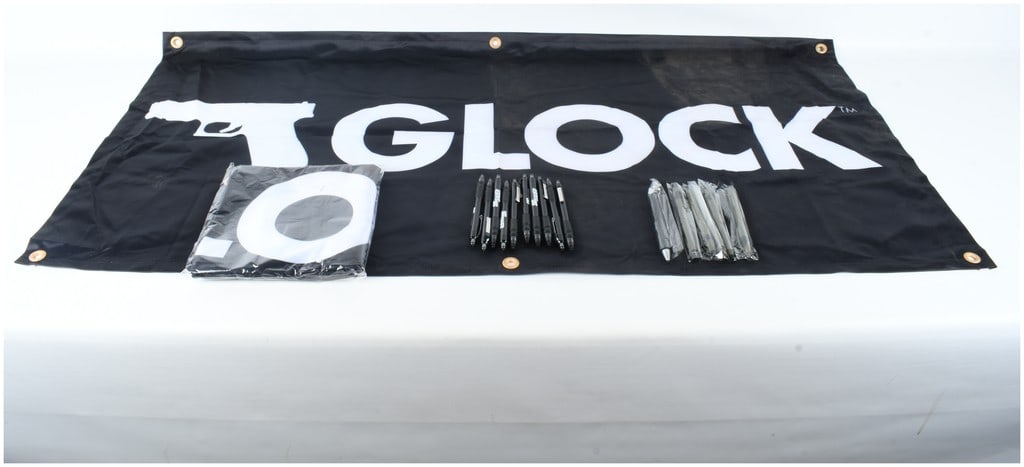 A Collection of Glock and Sig Sauer Promotional Merchandise Including Banners and Pens: An assortment of promotional items from firearms manufacturers Glock and Sig Sauer. The collection features a black fabric Glock retail banner, identified by web consensus as model AD02044, with