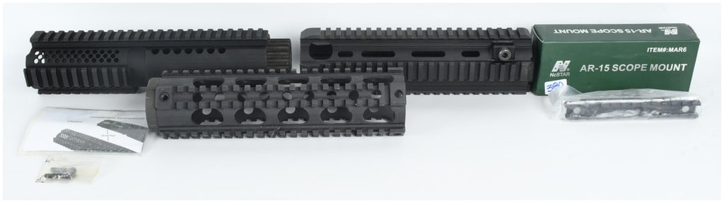 A Collection of Four AR-15 Handguards and Scope Mount: This lot consists of a collection of four AR-15 platform accessories, featuring three distinct quad-rail handguards and one boxed scope mount. The first handguard is a two-piece design with a matte bl