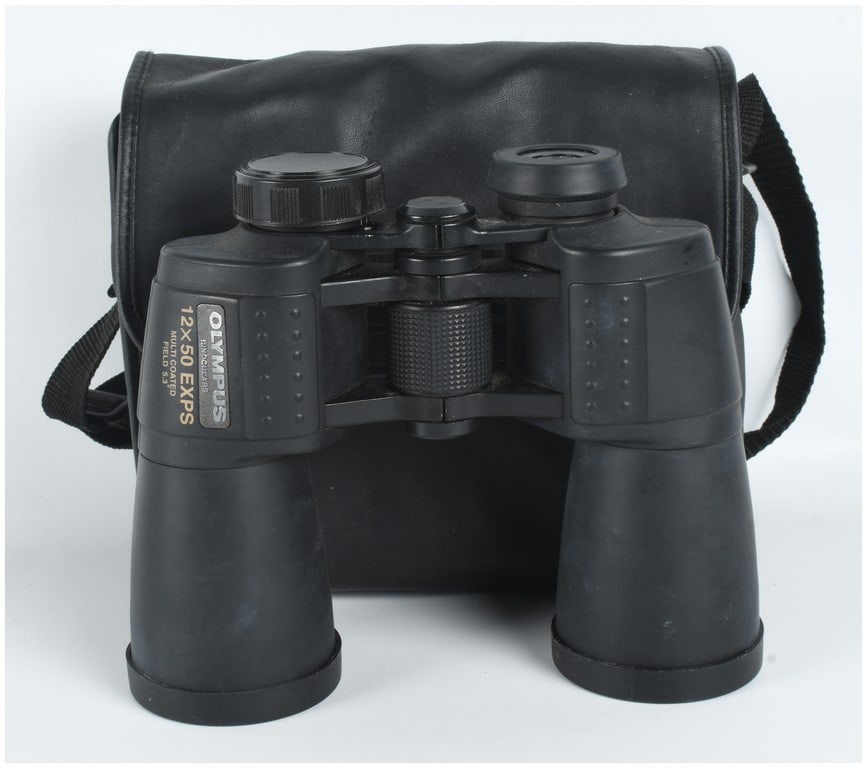 Olympus 12x50 EXPS Multi-Coated Porro Prism Binoculars: A pair of Olympus 12x50 EXPS multi-coated porro prism binoculars. The instrument features a black rubberized armor coating over a metal and plastic chassis with glass optics. The left prism housing be