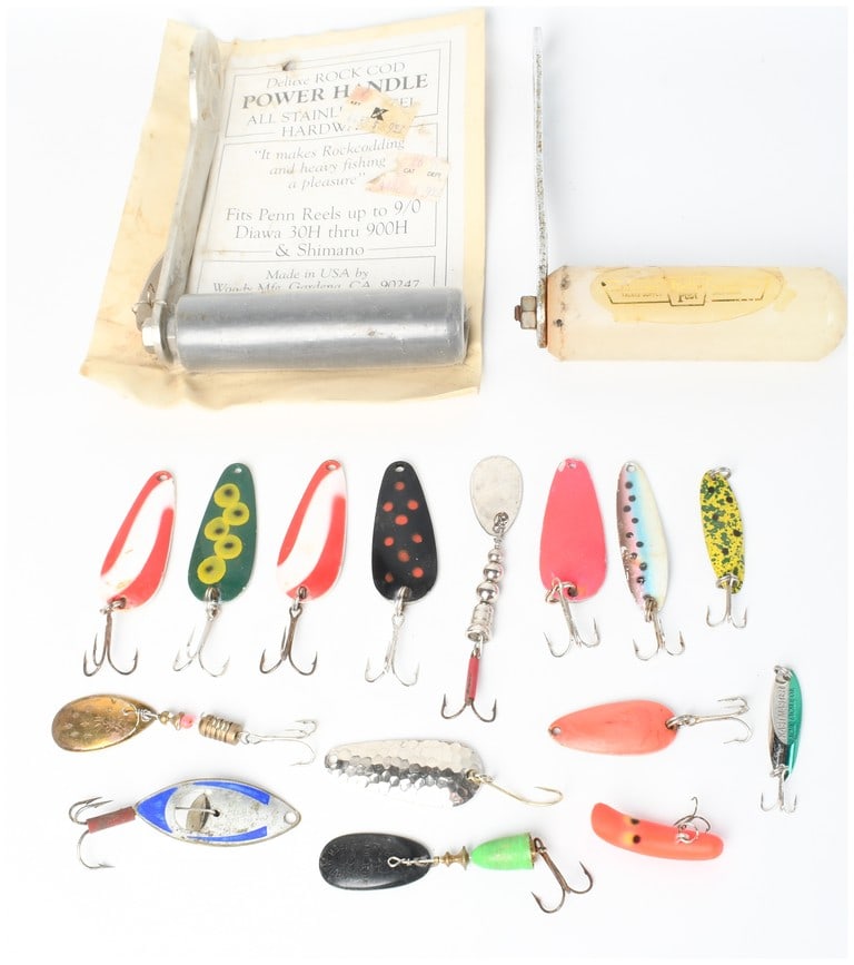 An Assortment of Vintage Fishing Lures and Reel Power Handles including Woody Mfg., Mepps, and Blue: This collection of vintage fishing tackle features two reel power handles and an assortment of artificial lures. One handle is a Deluxe Rock Cod Power Handle made of stainless steel by Woody Mfg. of G