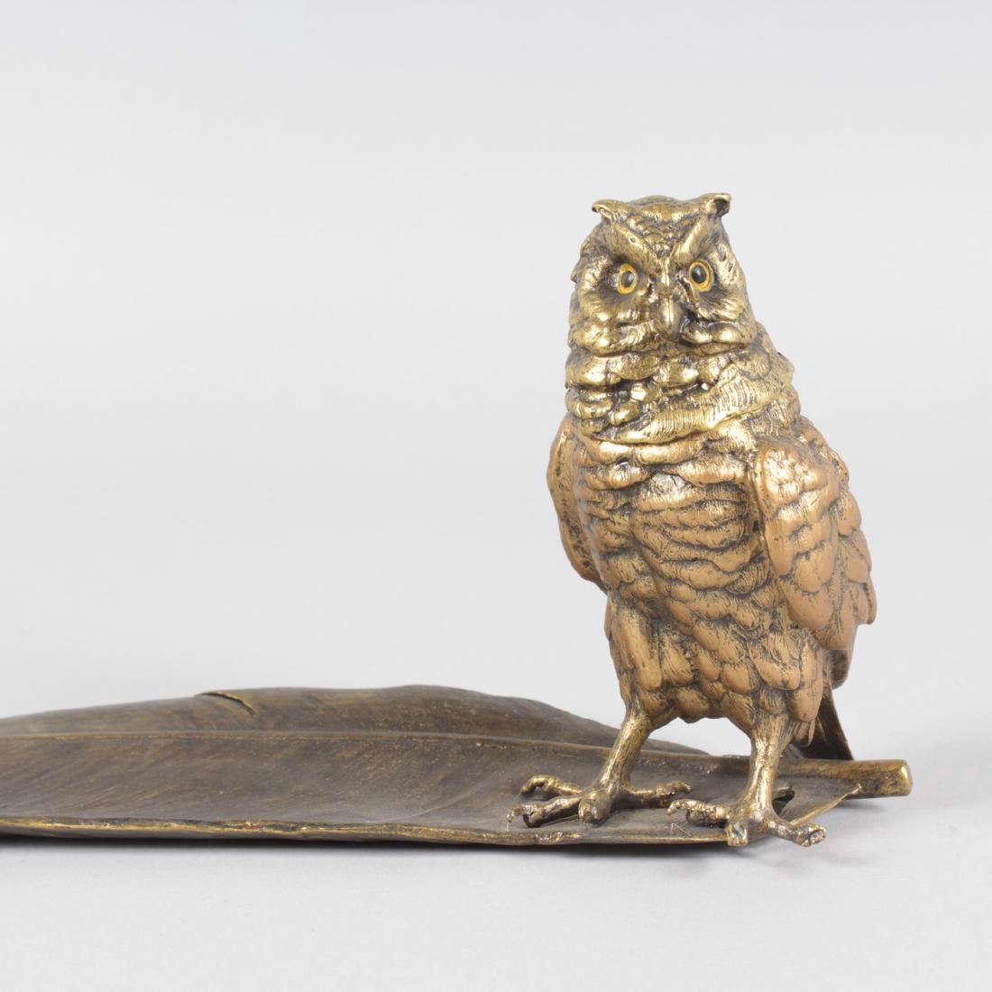 A COLD CAST BRONZE OWL INKWELL standing on a long: A COLD CAST BRONZE OWL INKWELL standing on a long feather. 13ins long.