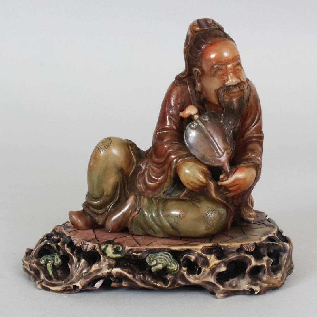 A CHINESE STAINED SOAPSTONE FIGURE OF A RECLINING SAGE, (1 of 7)