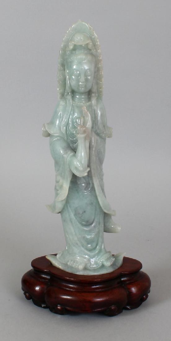 A CHINESE CELADON GREEN JADE FIGURE OF GUANYIN,: A CHINESE CELADON GREEN JADE FIGURE OF GUANYIN, together with a fitted wood stand, 13.5in(34.3cm) high overall, the figure itself 11.75in(29.9cm) high.
