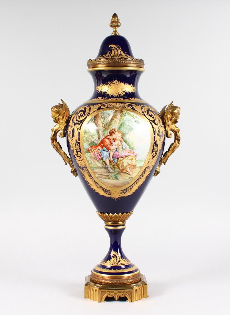 A GOOD SEVRES RICH BLUE TWO HANDLED URN AND COVER,: A GOOD SEVRES RICH BLUE TWO HANDLED URN AND COVER, edged in gilt with reverse panels painted with figures and a house, with ormolu mounts and female handles. 26ins high.