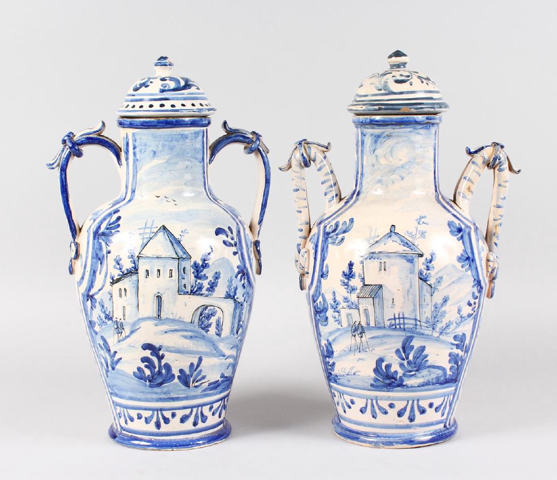 A LARGE PAIR OF DELFT BLUE AND WHITE TWO-HANDLED: A LARGE PAIR OF DELFT BLUE AND WHITE TWO-HANDLED POTTERY VASES AND COVERS painted with a town scene. 16ins high.