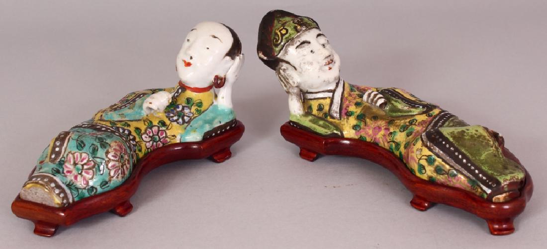 A PAIR OF JIAQING STYLE FAMILLE ROSE PORCELAIN: A PAIR OF JIAQING STYLE FAMILLE ROSE PORCELAIN RECLINING FIGURES, together with fitted wood stands, each base unglazed, the figures themselves 6.8in & 5.9in wide.