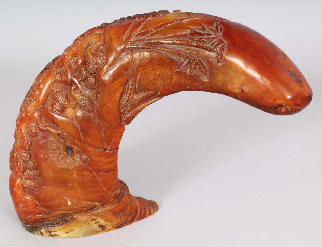 A CHINESE STAINED HORN TUSK CARVING, decorated in: A CHINESE STAINED HORN TUSK CARVING, decorated in relief with a scene of two sages in a grove of pine and bamboo, 6in high & 8in long.
