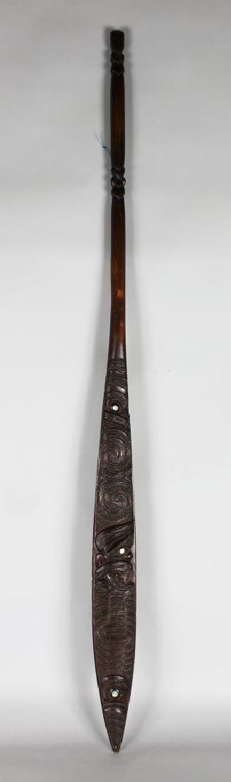 MAORI DANCE PADDLE Wood, paua shell, slender form with: MAORI DANCE PADDLE Wood, paua shell, slender form with cylindrical shaft and flat blade carved both sides with Koru and Pikorua designs. Length 54 ins. Note: Maori paddles, called hoe have a flat and 