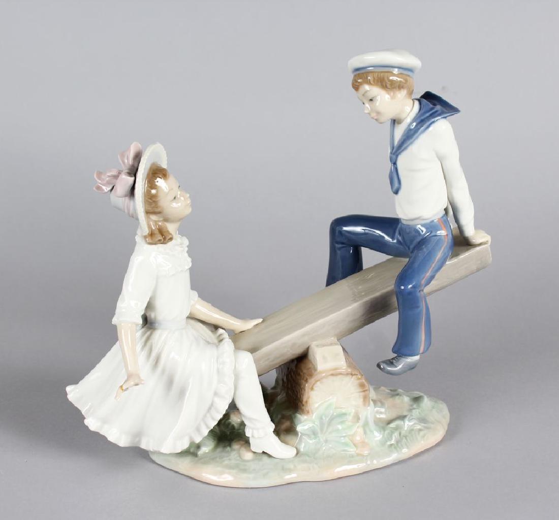 A LLADRO PORCELAIN GROUP "THE SEESAW", a young boy and: A LLADRO PORCELAIN GROUP "THE SEESAW", a young boy and girl on a seesaw. 11ins long, 9.5ins high.