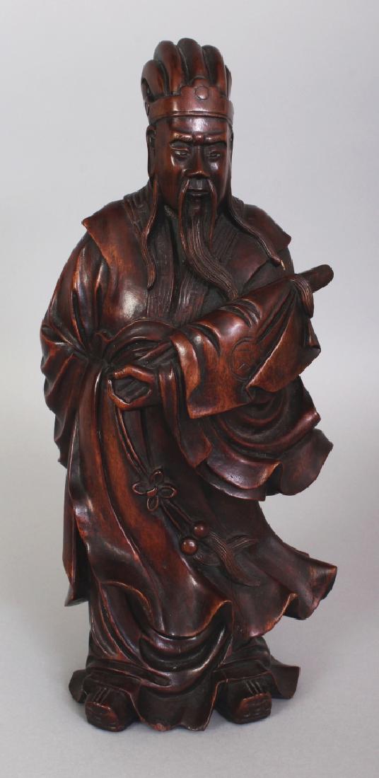 A CHINESE WOOD FIGURE OF A STANDING OFFICIAL, dressed: A CHINESE WOOD FIGURE OF A STANDING OFFICIAL, dressed in swirling robes and bearing a furled banner, 12in high.