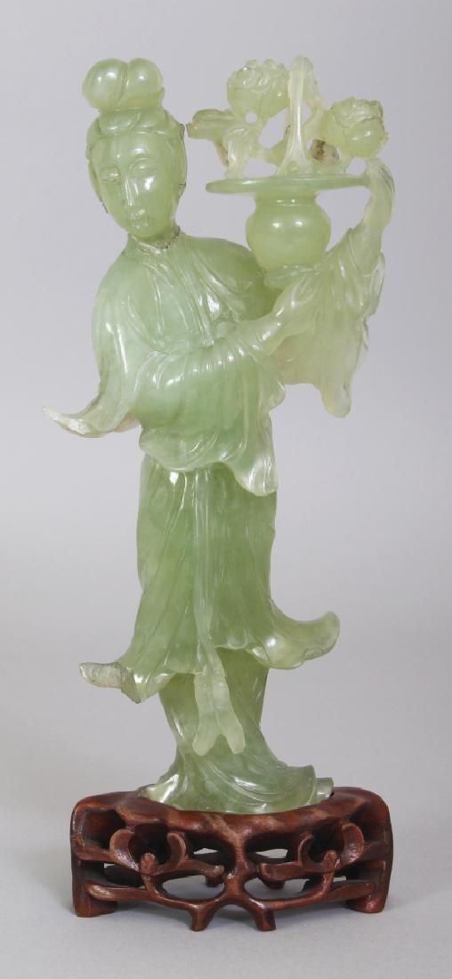 A 20TH CENTURY CHINESE CELADON GREEN BOWENITE CARVING: A 20TH CENTURY CHINESE CELADON GREEN BOWENITE CARVING OF A STANDING LADY, together with a fitted wood stand, the lady bearing aloft a basket of flowers, 9in high overall, the carving itself 7.8in high