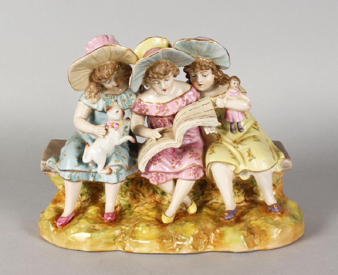A CONTINENTAL PORCELAIN GROUP OF THREE YOUNG GIRLS,: A CONTINENTAL PORCELAIN GROUP OF THREE YOUNG GIRLS, reading a book, a cat on one lap and sitting on a bench. 11ins long.