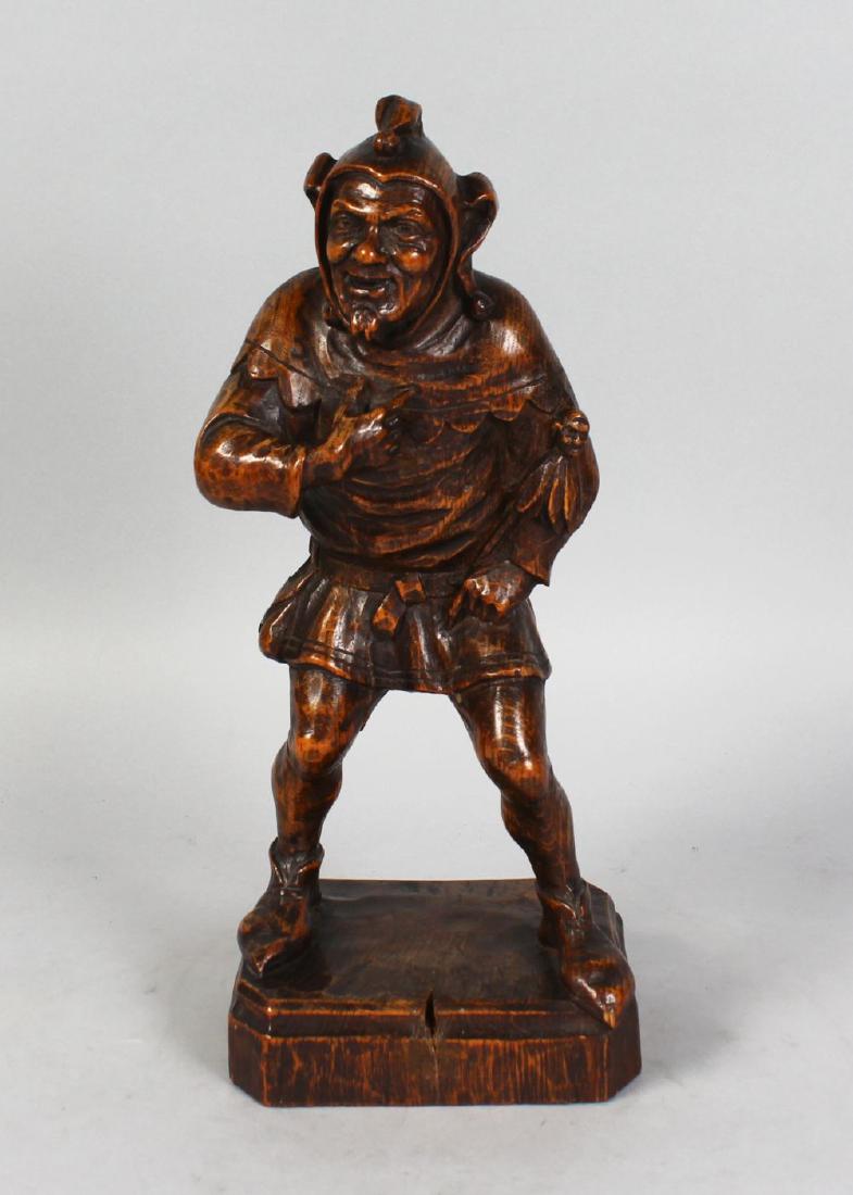 A GOOD BLACK FOREST CARVED WOOD FIGURE OF A JESTER,: A GOOD BLACK FOREST CARVED WOOD FIGURE OF A JESTER, standing on a rectangular base. 13ins high.