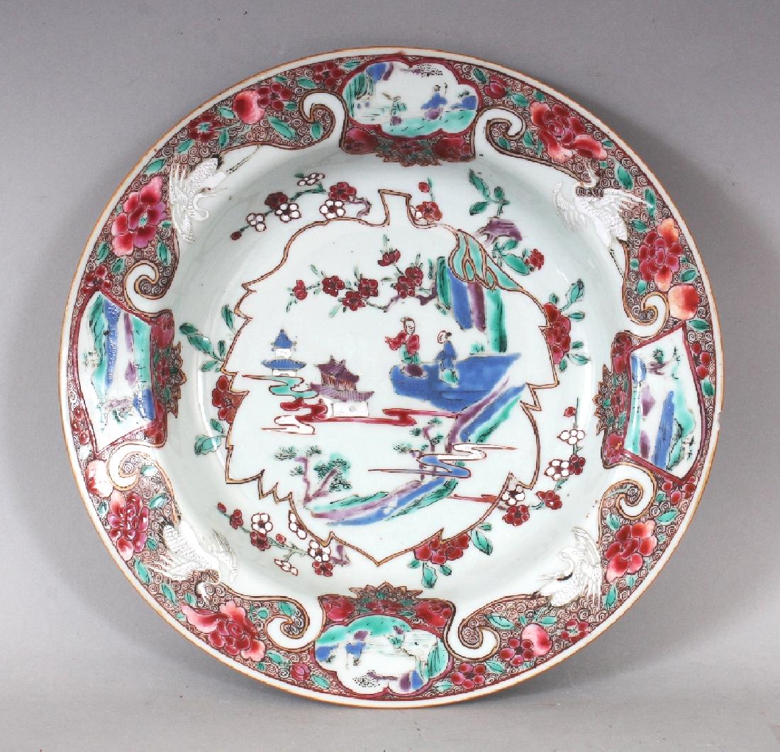 A CHINESE YONGZHENG PERIOD FAMILLE ROSE PORCELAIN SOUP: A CHINESE YONGZHENG PERIOD FAMILLE ROSE PORCELAIN SOUP PLATE, circa 1730, painted with a leaf-form panel to its centre, the flanged rim with storks and vignettes, 8.9in diameter.