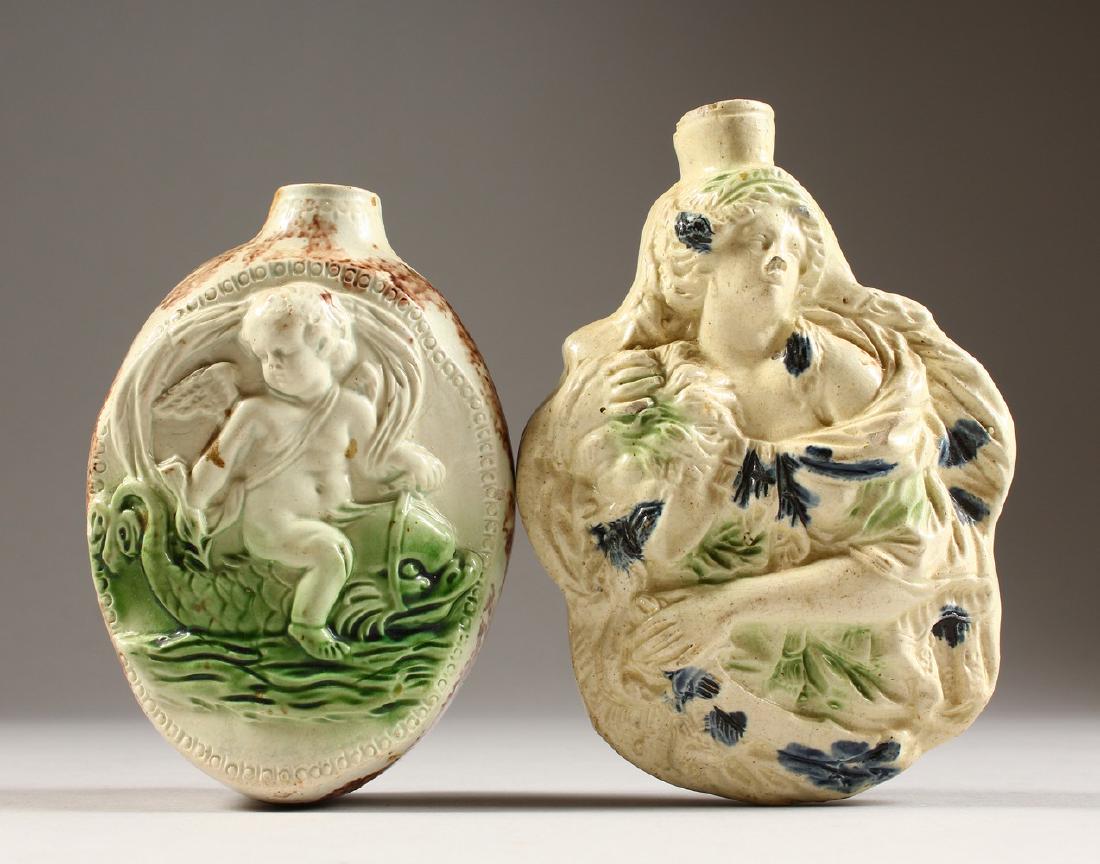 TWO 19TH CENTURY WHIELDON TYPE FLASKS, each with: TWO 19TH CENTURY WHIELDON TYPE FLASKS, each with moulded decoration, one as a double sided female holding a severed head, the other with a sleeping lady and a putti riding a dolphin. 5ins and 5.5ins h