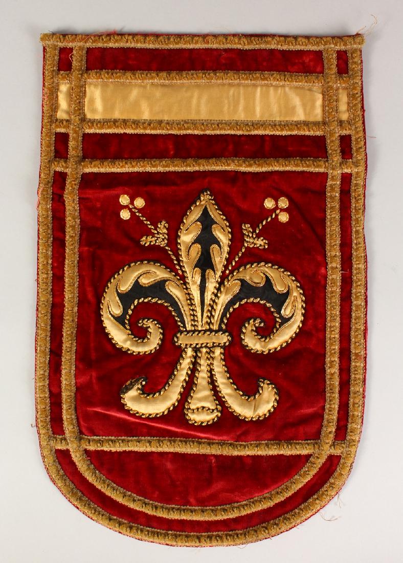 A RED VELVET PENNANT, embroidered with a single: A RED VELVET PENNANT, embroidered with a single fleur-de-lys design. 20ins x 13ins.